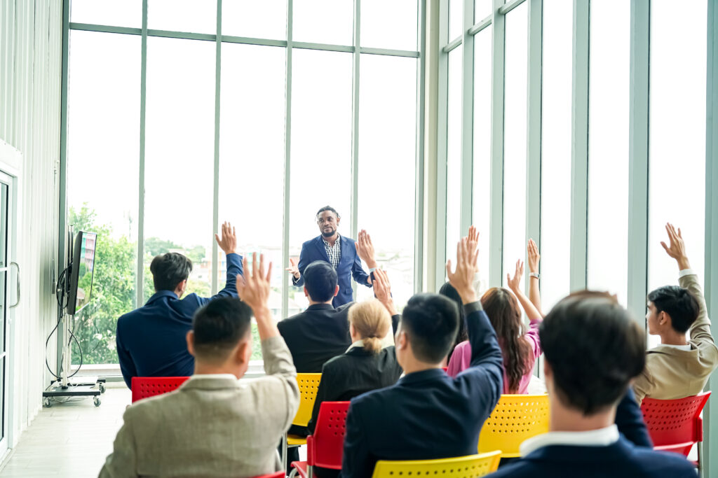 Raised up hands of large group in seminar class room to agree with speaker at conference seminar