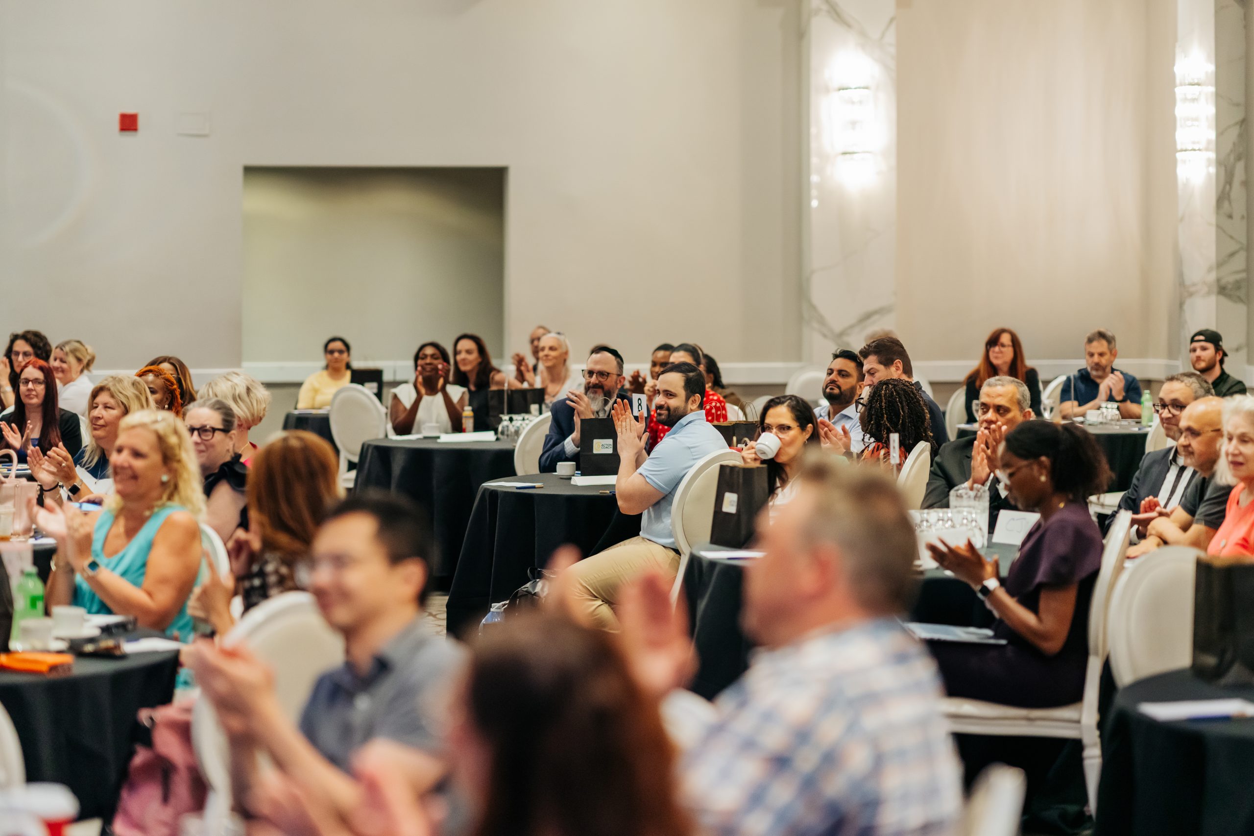 A conference room of business owners applauding at an ActionCOACH event