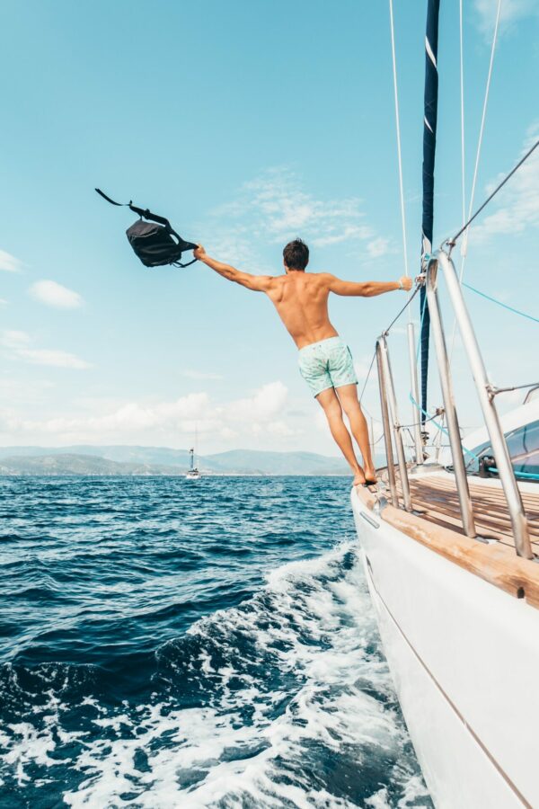 Man on sailboat throughing backpack overboard, symbolizing freedom
